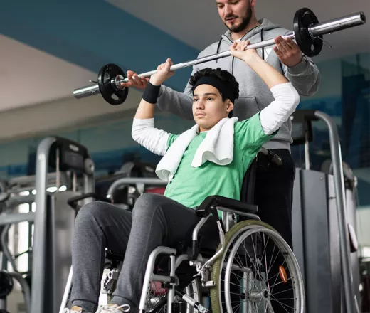Young Man in Wheelchair Lifting Weights with Trainer